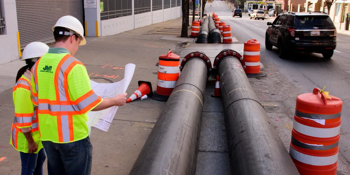 Field workers reading plans, pipes in road