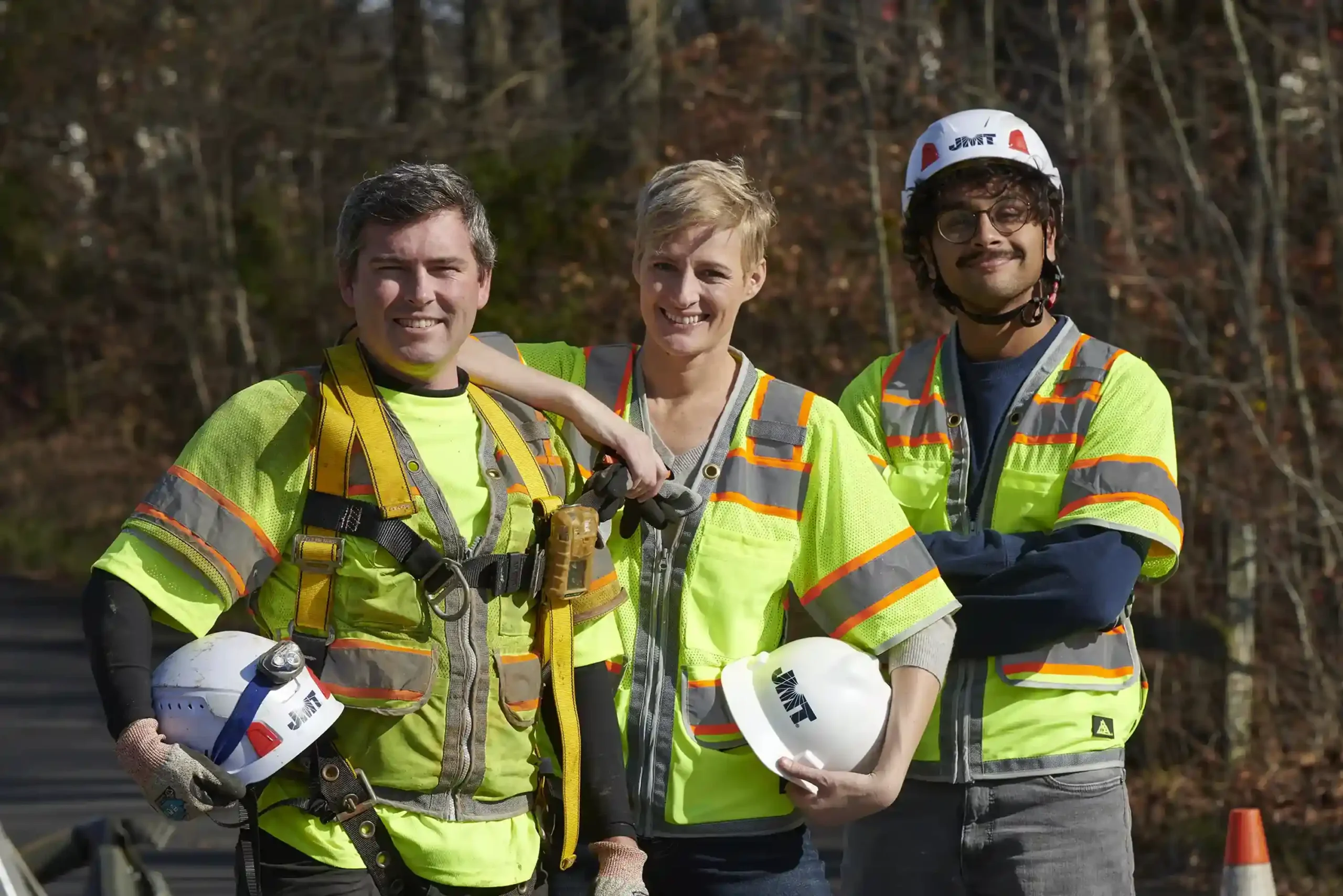 3 smiling JMT employees working in the field