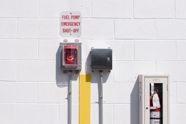 Emergency shut-off, small locked box, and fire extinguisher adhered to a white brick wall
